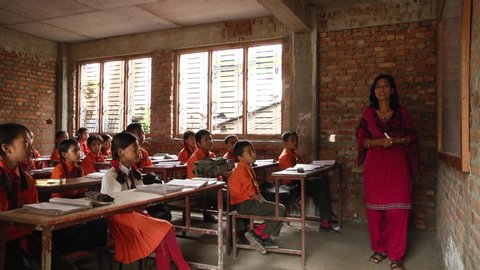 Kathmandu / Nepal - 04 27 2019: Students sitting in Kathmandu, Nepal classroom dressed in orange uniforms listening in lesson to teacher standing at the front of class, writing on board.