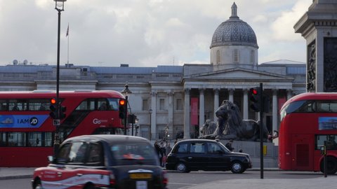 London / United Kingdom (UK) - 04 25 2019: Busy street view of iconic red double decker bus and black cab taxis driving past the National Gallery in Trafalgar Square.