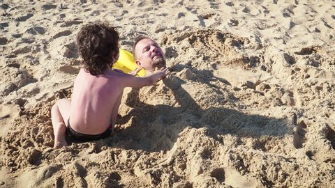 4K Father Plays With His Little Boy At Beach, Little Son Is Buried In Sand, Cute Moment Slow Motion