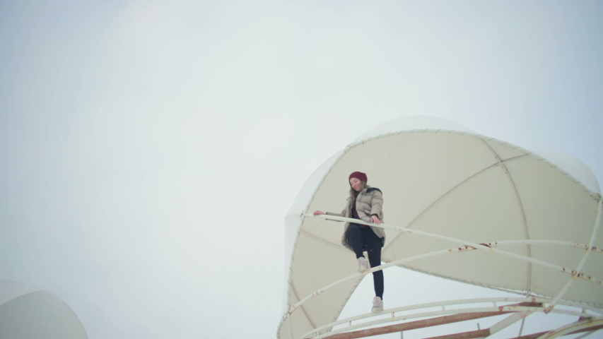 low angle shot beautiful girl stands on disassembled tent dome edge stretches hands under clear sky in snowy weather