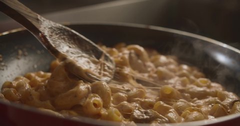 Chef is mixing pasta with mushrooms and cheese in skillet with wooden spoon. 4K Slow Motion video