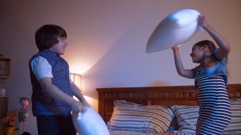 Two young adorable Indian children enjoying and having fun at night - playful kids. Siblings fighting with a pillow and having fun at home before sleeping - night fight. 