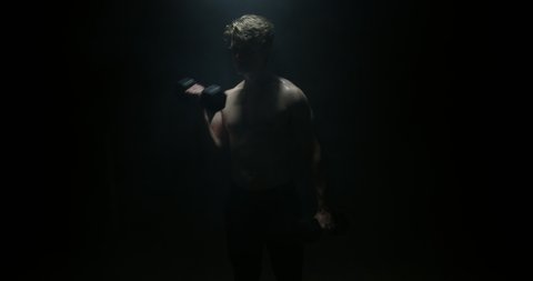 Male Model In A Dark Background Lifting Weights Away From The Camera On Spotlight Preparing For Big Match Wearing White T-shirt