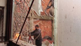 View trough broken window on worker who is cutting small tubes, obsolete industrial equipment with acetylene torch. H.264 video codec