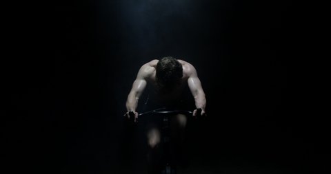 Exercising On Exercise Bike Shirtless Towards Camera Training As Smoke Falls On Him In A Dark Background