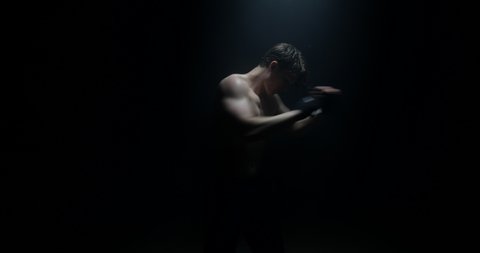 Male Boxer In Dark Background Sparring Away From Camera Training for Big Boxing Match Shirtless With Spotlight On Him