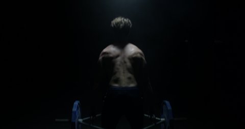 Shirtless Male Weightlifter With The Back To The Camera And Lifting Weights In A Dark Background
