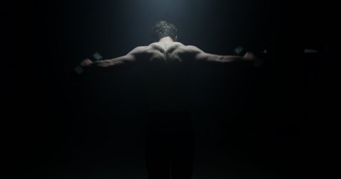 Athletic Male With His Back To The Camera In A Dark Background Lifting Weights On Spotlight Preparing For Big Match