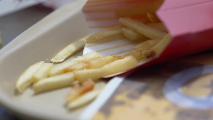 Close up of fries in a container on a tray a Caucasian hand comes in and grabs a few fries ready to eat this meal for lunch. Royalty-Free Stock Footage #1034816051