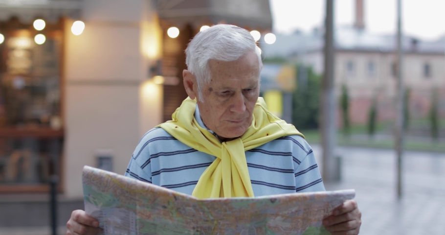 Senior male tourist exploring town with a map in hands and looking for the route while traveling in Lviv, Ukraine. A man in t-shirt and sweater that is tied around his neck. Vacation concept
