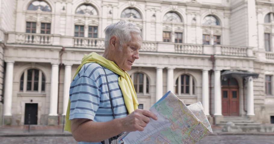 Senior male tourist asking woman for directions in town using a map in hands. Looking for the route while traveling in Lviv, Ukraine. Elegant old adult woman in hat helps him