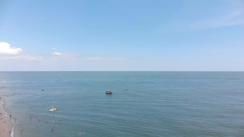 The boat sails on the sea. People sunbathe on the beach. Aerial view of beach and sea. Wave on the sea, ocean. Beach. Quadcopter.