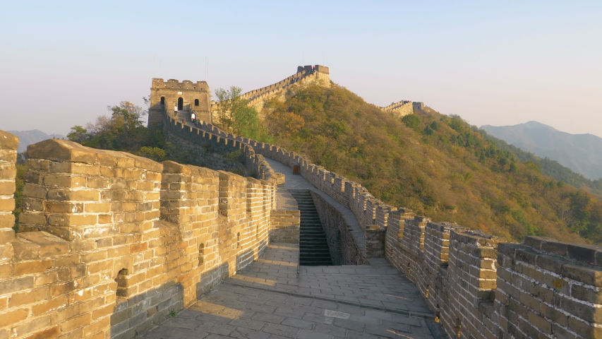 Stone stairwell leads up to the path on top of the majestic Great Wall of China. Stunning view of the ancient stone wall in rural China illuminated by the golden evening sun. Great Wall at sunrise. Royalty-Free Stock Footage #1034821331