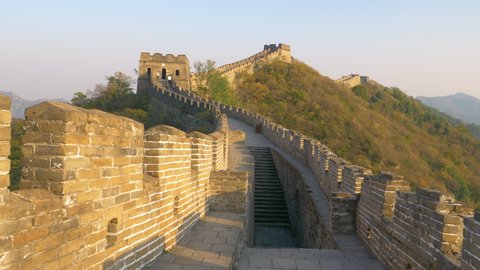 Stone stairwell leads up to the path on top of the majestic Great Wall of China. Stunning view of the ancient stone wall in rural China illuminated by the golden evening sun. Great Wall at sunrise.