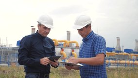 teamwork. industry gas production station concept. slow motion video. two engineers in helmets are studying working with a digital tablet in a factorygas supply business contract. two workers work at