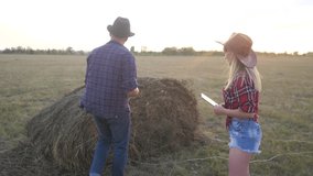 teamwork happy family smart farming concept slow motion video. girl and man agronomist holds digital tablet touch pad computer teamwork in field with haystacks grass is studying and examining crops