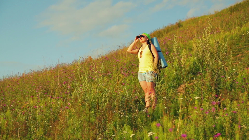 Woman hiker on a hill with a backpack behind her, looking through binoculars
