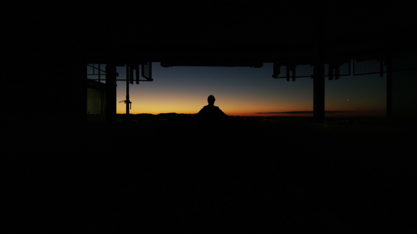 Silhouette of constuction worker in hardhat watching sunrise then walking onto site