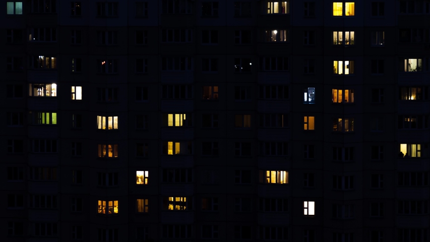 Time laps video of night windows in an urban multi-story apartment building. The light in the windows lights up and goes out.
