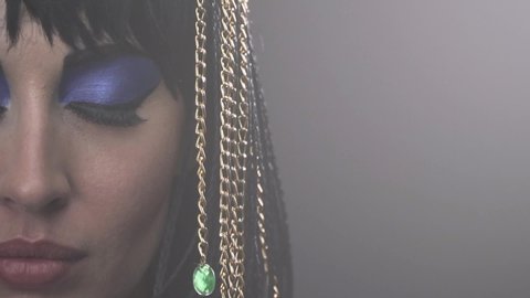 Cleopatra is opening her eyes, bright blue makeup and jewelry in her hair