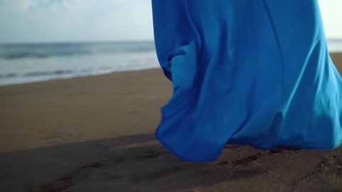 Woman in beautiful blue dress walking along a black volcanic beach. Slow motion