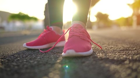 Close up of woman tying shoe laces and running along the palm avenue at sunset