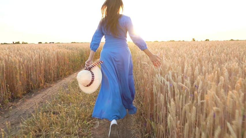 Beautiful woman in a blue dress and hat runs through a wheat field at sunset. Freedom concept. Wheat field in sunset. Slow motion Royalty-Free Stock Footage #1034843759