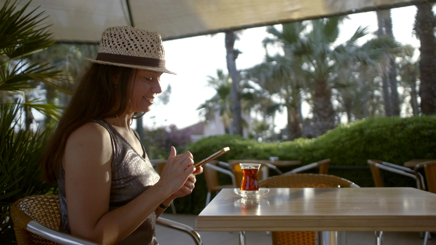 Adult attractive woman reading news on social networks and drinking Turkish tea, sitting in the hotel restaurant