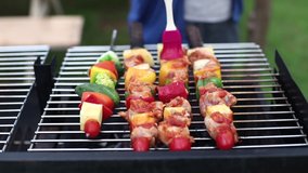  A woman's hands rotating the skewers of barbecue being fried on a charcoal grill, barbecue party in the garden backyard