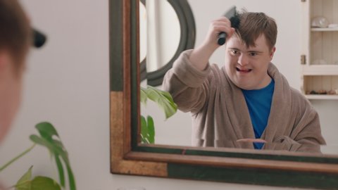 funny teenage boy with down syndrome dancing in bathroom having fun brushing hair enjoying morning routine getting ready wearing bathrobe