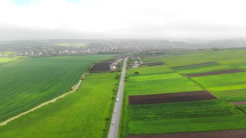 Aerial Flying over the road with cars separating the green fields. Foggy day and the Route that connects the city