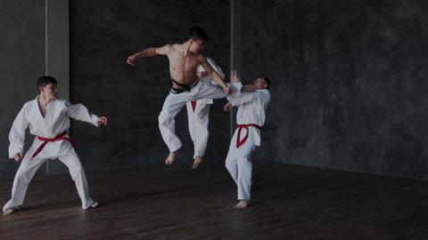 Brave powerful asian guy fighting alone against three strong warriors in white kimono. He perform active martial tricks and makes forceful attack. Slow motion and rapid. Part 1.