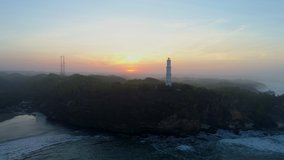 Cinematic parallax aerial footage lighthouse view from drone flying forward slowly approaching lighthouse on rock cliff and golden sky background in misty