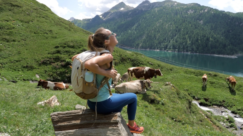 Hiking woman resting on rock above alpine lake on mountain trail contemplating the beautiful landscape in Switzerland; Girl hiking enjoys Summer outdoor activities 