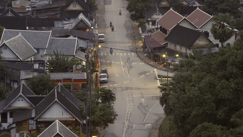 Close up High angle view of road light traffic on it lit up with street lights surrounded by houses and buildings on either side in Luang Prabang, Laos