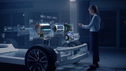 Female Automobile Engineer Using Digital Tablet with Augmented Reality Analyses Electric Engine Prototype. Innovative Facility: Vehicle Frame with Graphics Showing Motor Parts, Torque and Infographics