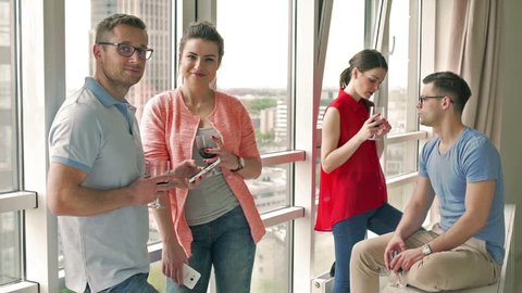Couple smiling to the camera while drinkig wine in the apartment
