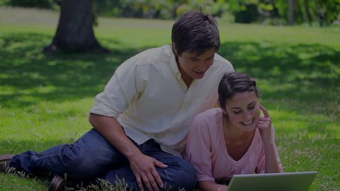 Animation of happy Cucasian couple lying on grass outdoors using a laptop computer while an empty icon of a house fills with blue