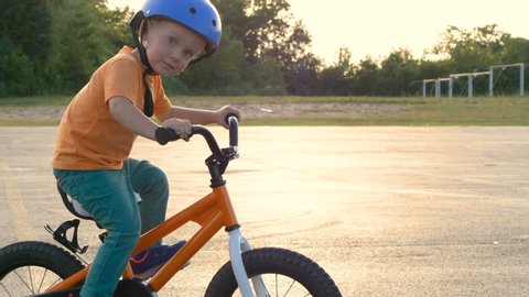 Cute little boy ( two years old child) is riding bike. Kid in orange t-shirt and blue helmet. Orange kids bicycle. First experience, childhood memories