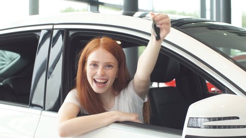 Happy ginger woman smiling at camera and showing new car key. Car Purchase or Rent concept
