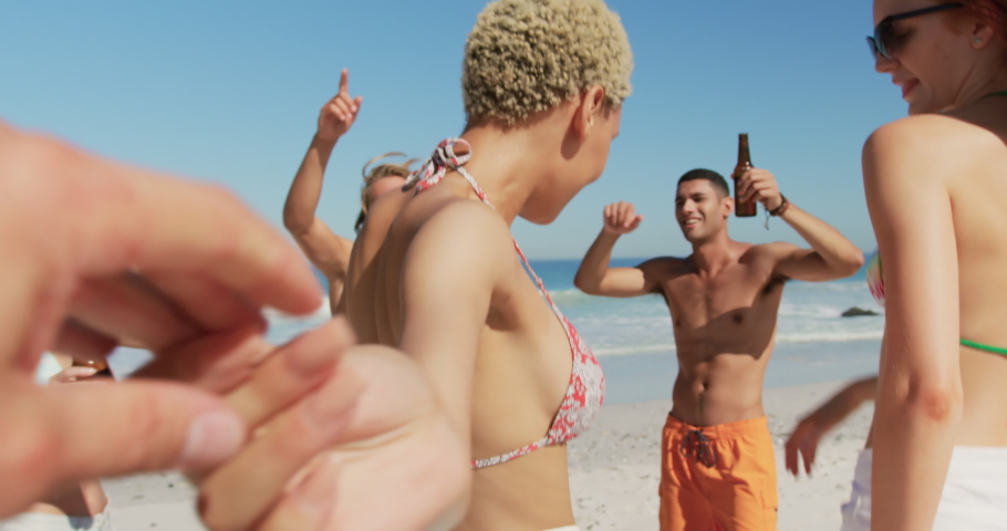 Point of view close up of holding the hand of a young mised race woman, who joins her multi-ethnic young adult friends dancing on a beach. Young friends having summer fun on the beach together 4k