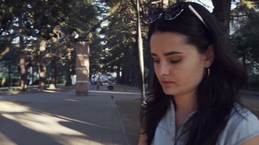 A beautiful girl sits in the park,wearing lipstick and puts on sunglasses.