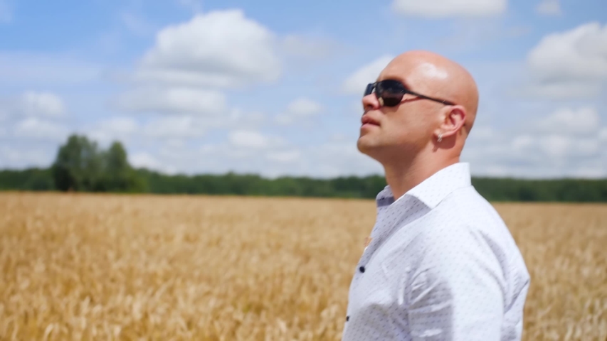 Side view of bald man going and singing in the golden wheat field. Medium shot.