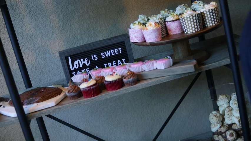 Slow Motion shot of a dessert table at a wedding reception. The shelf has fudge, cupcakes, macaroons, cookies, etc...