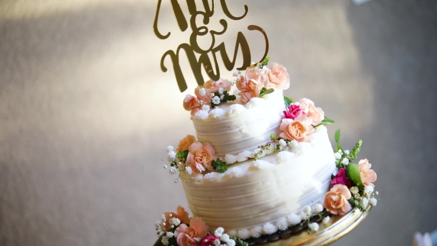 Smooth shot of a beautifully decorated wedding cake on a fancy platter at a wedding reception.
