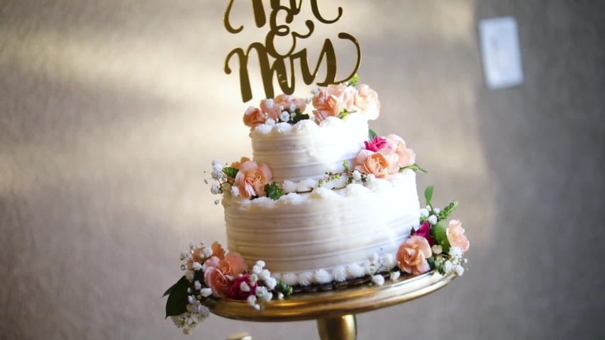 Smooth shot of a beautifully decorated wedding cake on a fancy platter at a wedding reception.