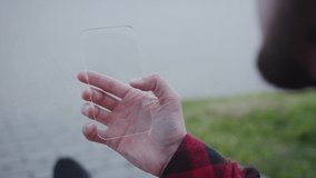 Hands man holding futuristic transparent smartphone in hand browsing on mobile phone with holographic screen visual effects outdoors in the street modern tech communication innovation slow motion - Powered by Shutterstock - Get 15% off with code: PIKWIZARD15