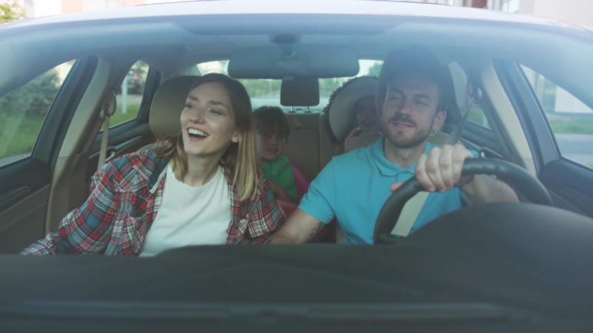 Front view of happy loving parents and their excited kids smiling driving a car in the city. Young family traveling abroad by car in summer. Royalty-Free Stock Footage #1034878295