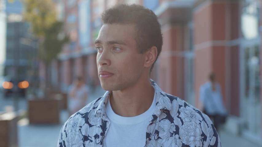 face portrait of attractive mixed race young man in stylish look smiling of joy walking in the beautiful city center on summer sunny day.