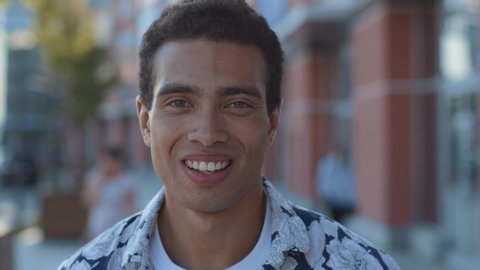 face portrait of attractive mixed race young man in stylish look smiling of joy walking in the beautiful city center on summer sunny day.